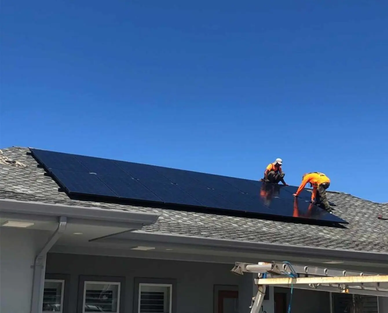 Two men installing solar panels on the roof of a house in, house has windows and a ladder